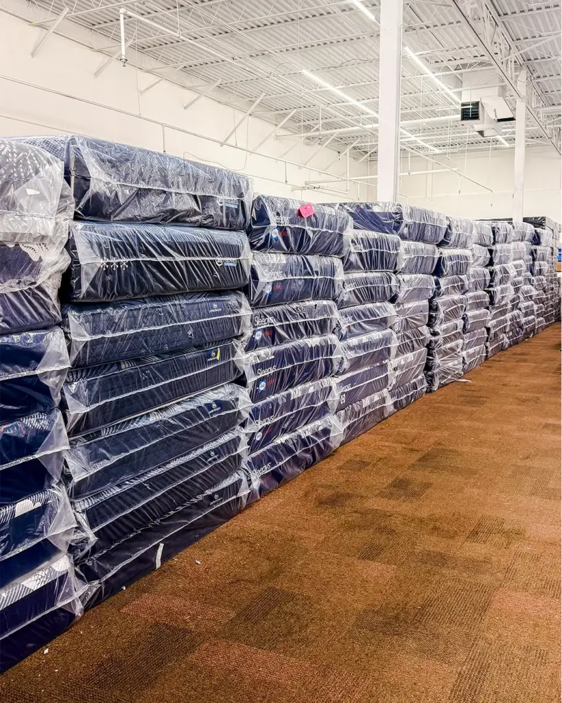 Warehouse wall of wrapped mattresses at Compare Deals mattress outlet